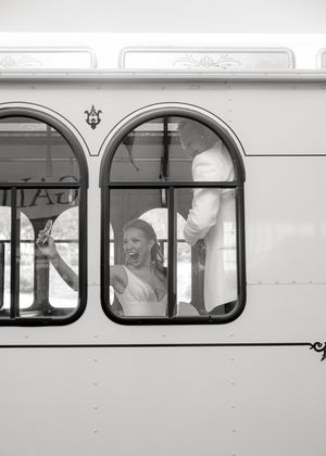 Black and white photo of people cheerfully waving from vintage trolley windows.