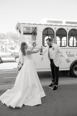 A couple dancing joyfully next to a vintage white trolley bus on their wedding day.