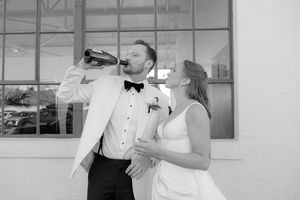 Bride and groom in formal attire celebrating with champagne against an industrial backdrop.