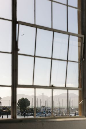 View of a marina with sailboat masts and mountains through a large industrial window frame.