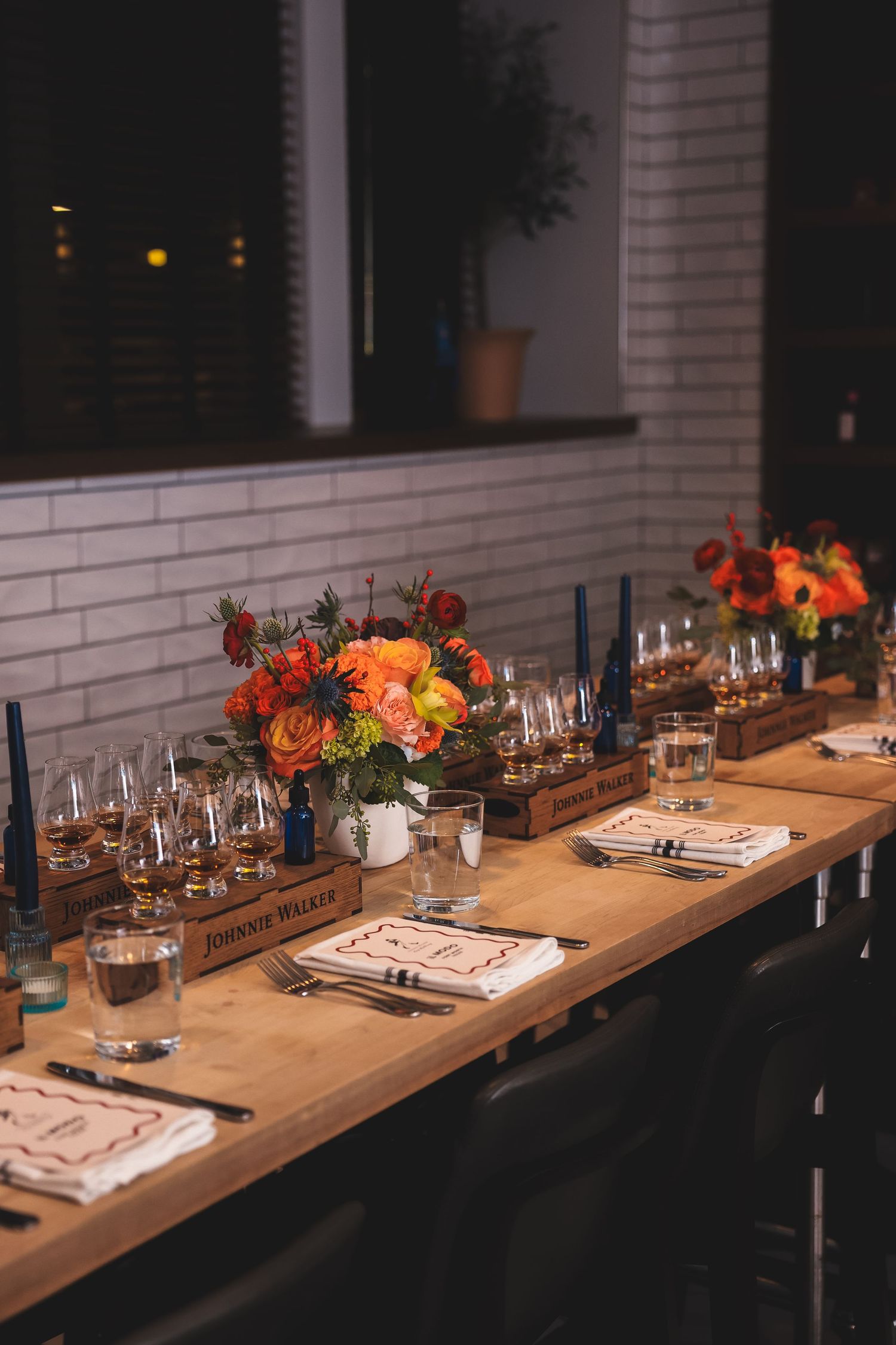 Elegantly set dinner table with orange floral centerpiece and place settings in a modern restaurant.