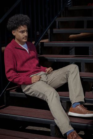 A person in a red zip-up sweater relaxes on dark wooden steps wearing brown casual shoes.