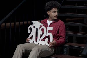 Person in a burgundy hoodie sitting on stairs while holding numbers showing 2025.