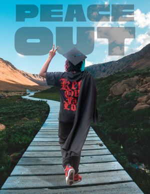 Graduate in cap and gown flashing peace sign on wooden boardwalk trail through scenic mountain valley.