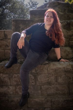 Person in black clothing lounges on stone wall in artistic outdoor photo series.