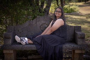 A person wearing a black dress reclines on a stone wall in a park setting during a photo session.