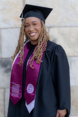 A graduate wearing a black cap and gown with a purple graduation stole smiles during commencement ceremonies.