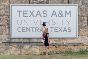 A stone wall with multiple university signs mounted on it including Texas A&M and Central Texas.