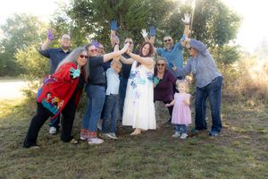 Large group of wedding guests pose together for a fun outdoor photo series on a grassy hillside.