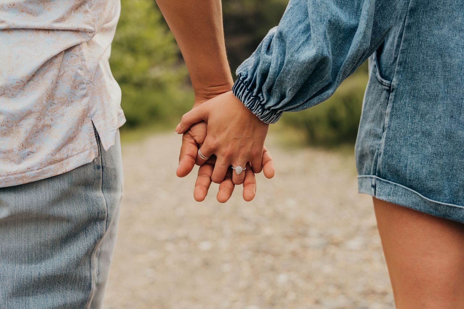 Close-up view of two people holding hands while walking on a gravel path together during their engagement session in Broken Bow, Ok.