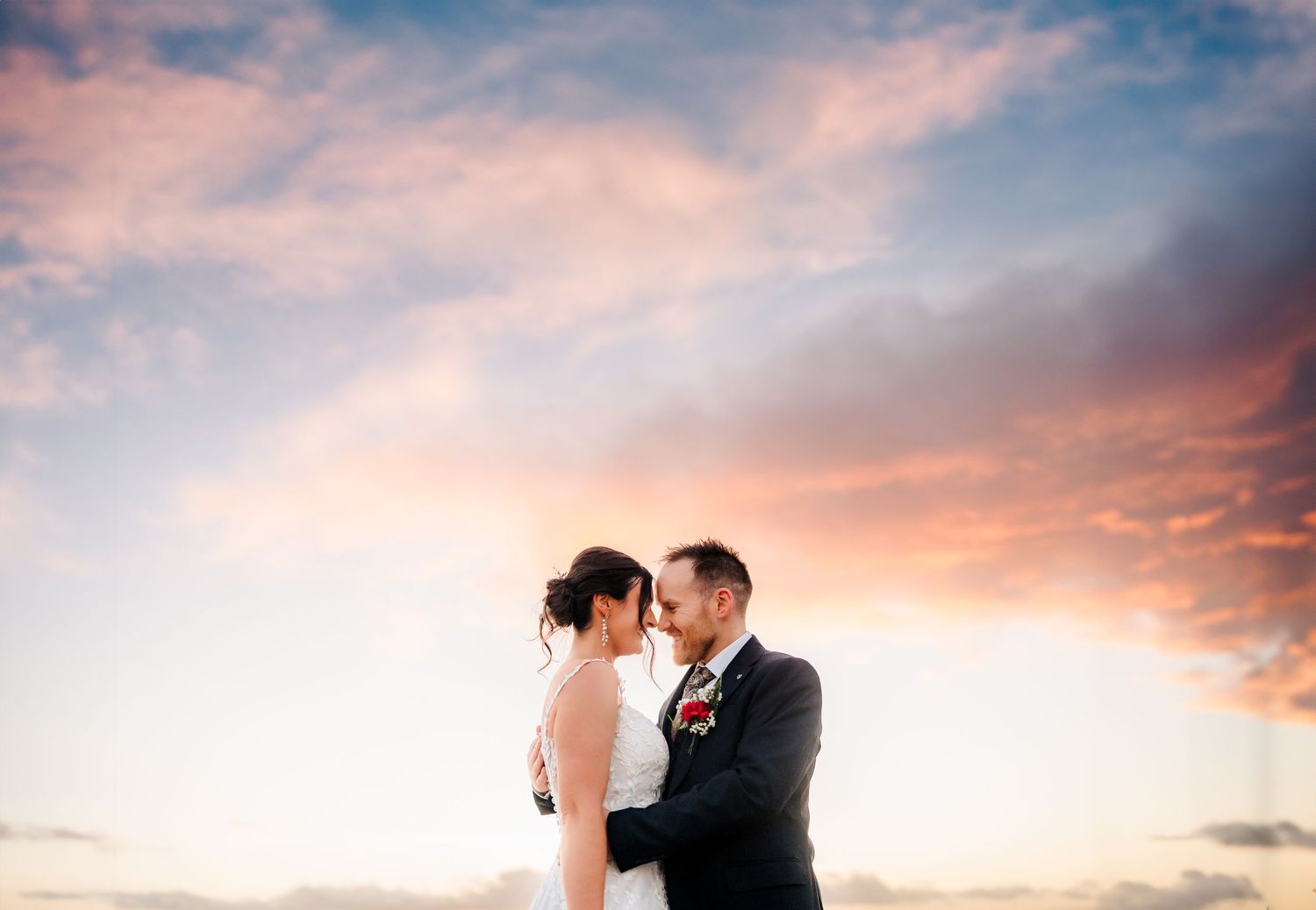 A romantic silhouette of newlyweds embracing against a vibrant sunset sky with pink and orange clouds.