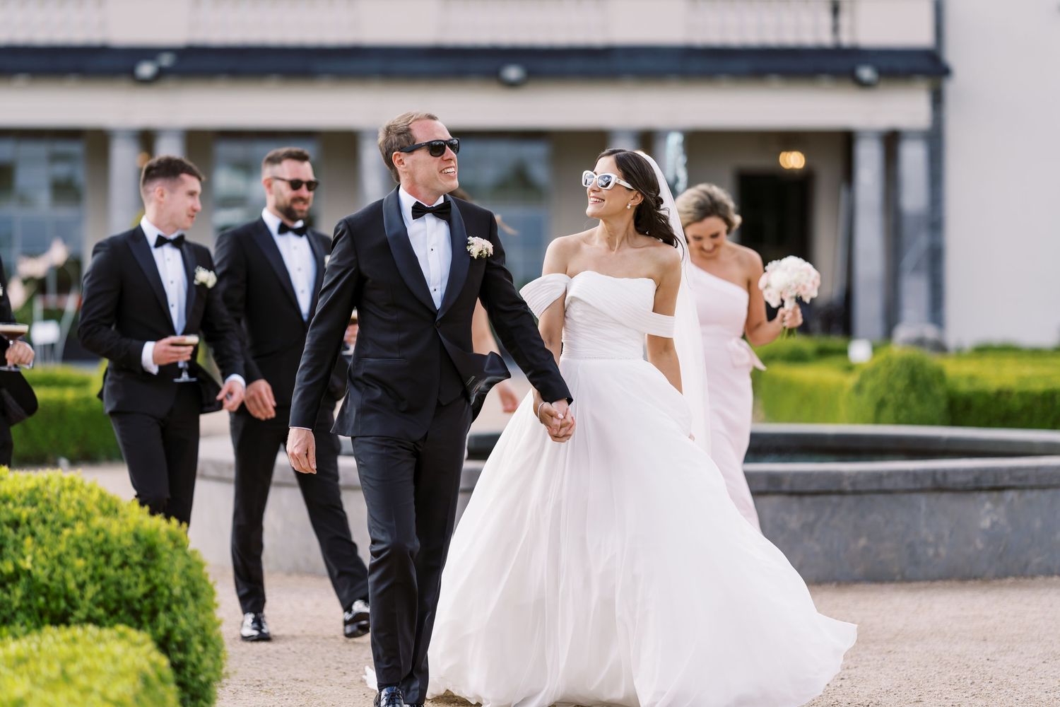 A wedding party walks together outdoors, with the couple leading the procession.