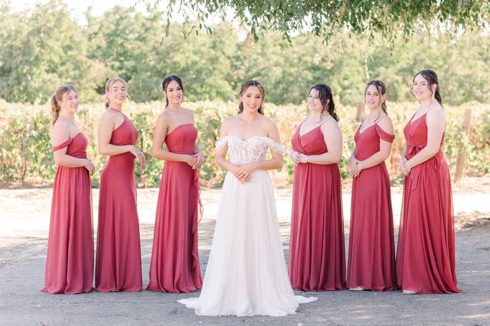 Wedding party in white and burgundy dresses poses together in a garden setting.