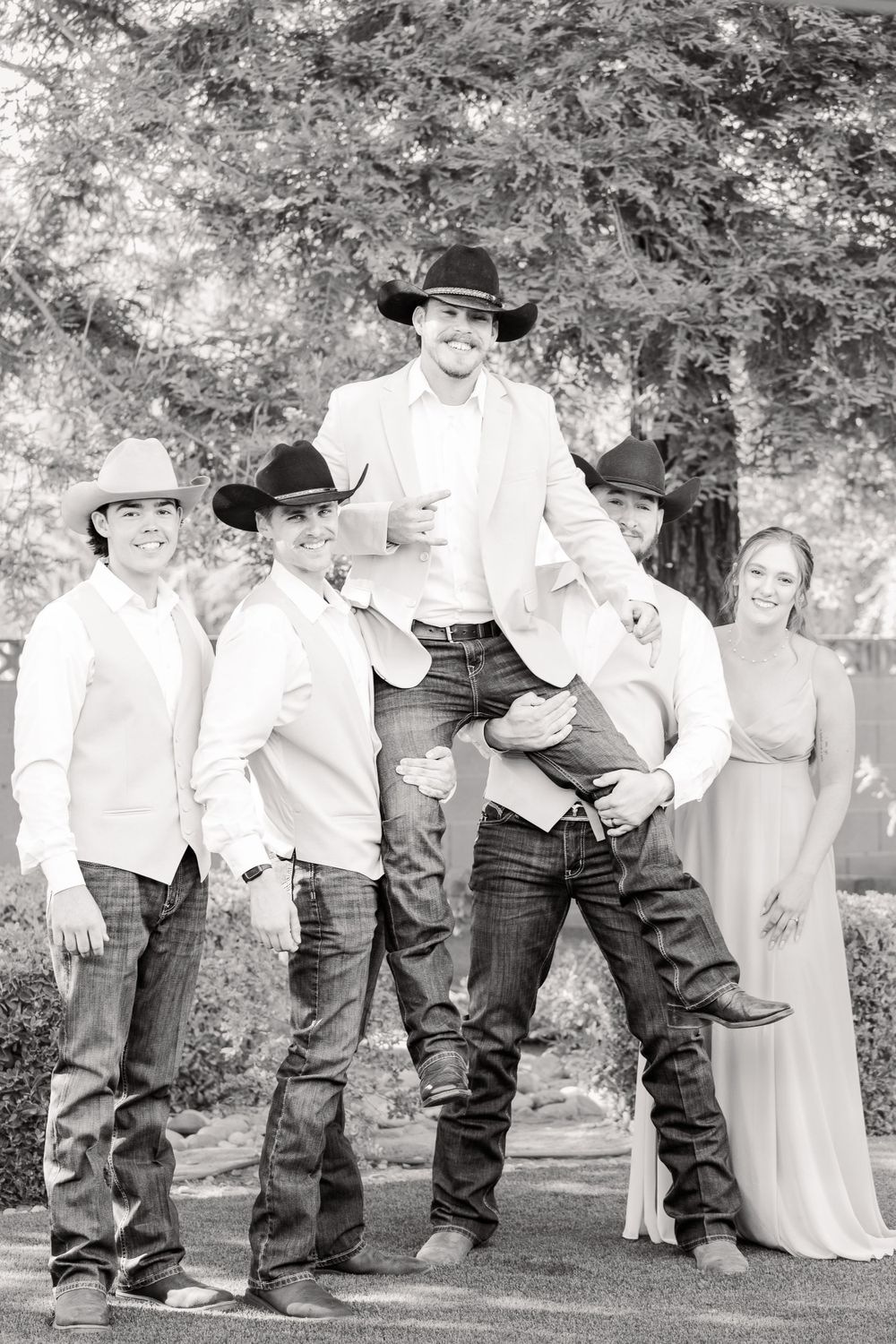 Groomsmen in western wear and cowboy hats pose playfully in black and white photography.
