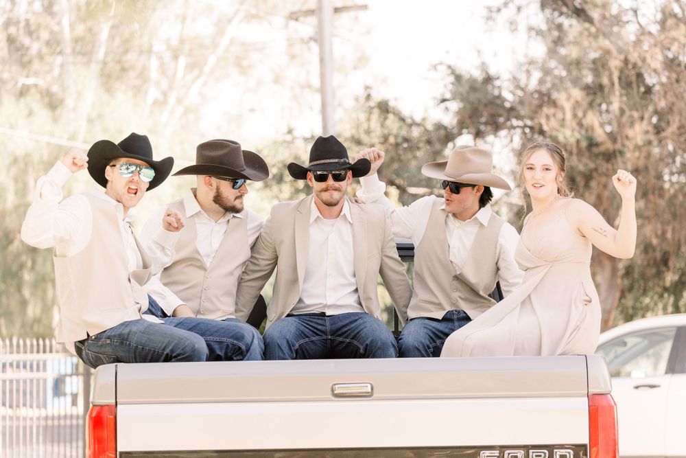 Groomsmen in cowboy hats and western attire pose casually on a bench outdoors.