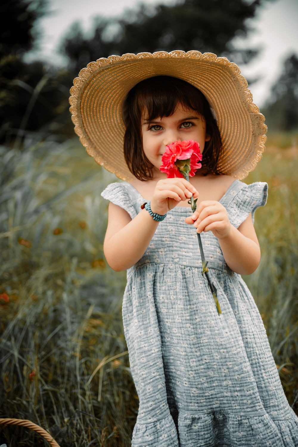 Spring outdoor natural light session with toddler in a sunhat smelling a carnation