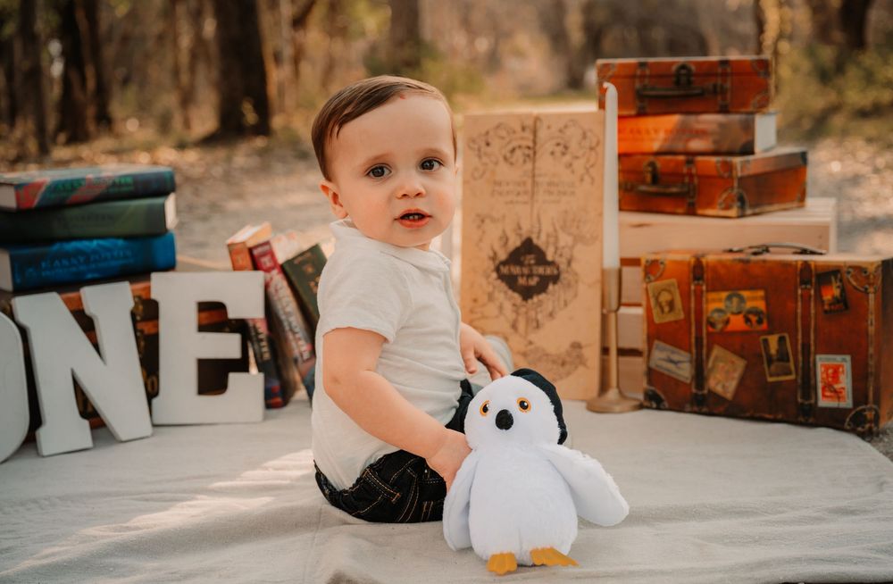 Baby sitting on blanket holding stuffed owl during first birthday harry potter themed session in Fort Worth
