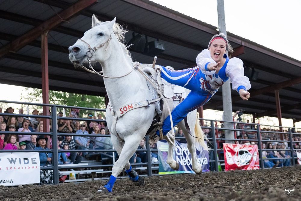 White horse and rider performing tricks during a rodeo show with crowd watching.  Nebraska Pro Rodeo PRCA Rodeo Photographer Dakota Cardenas