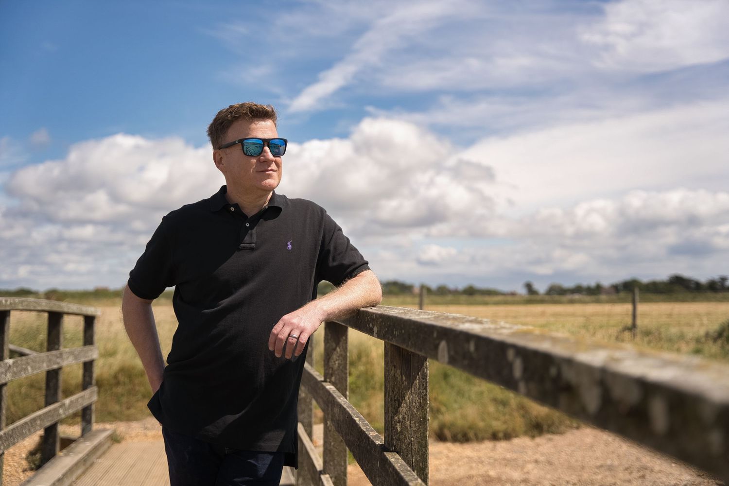 Dorset business owner leans on a wooden fence during a personal branding photoshoot on a sunny day in Milford On Sea.