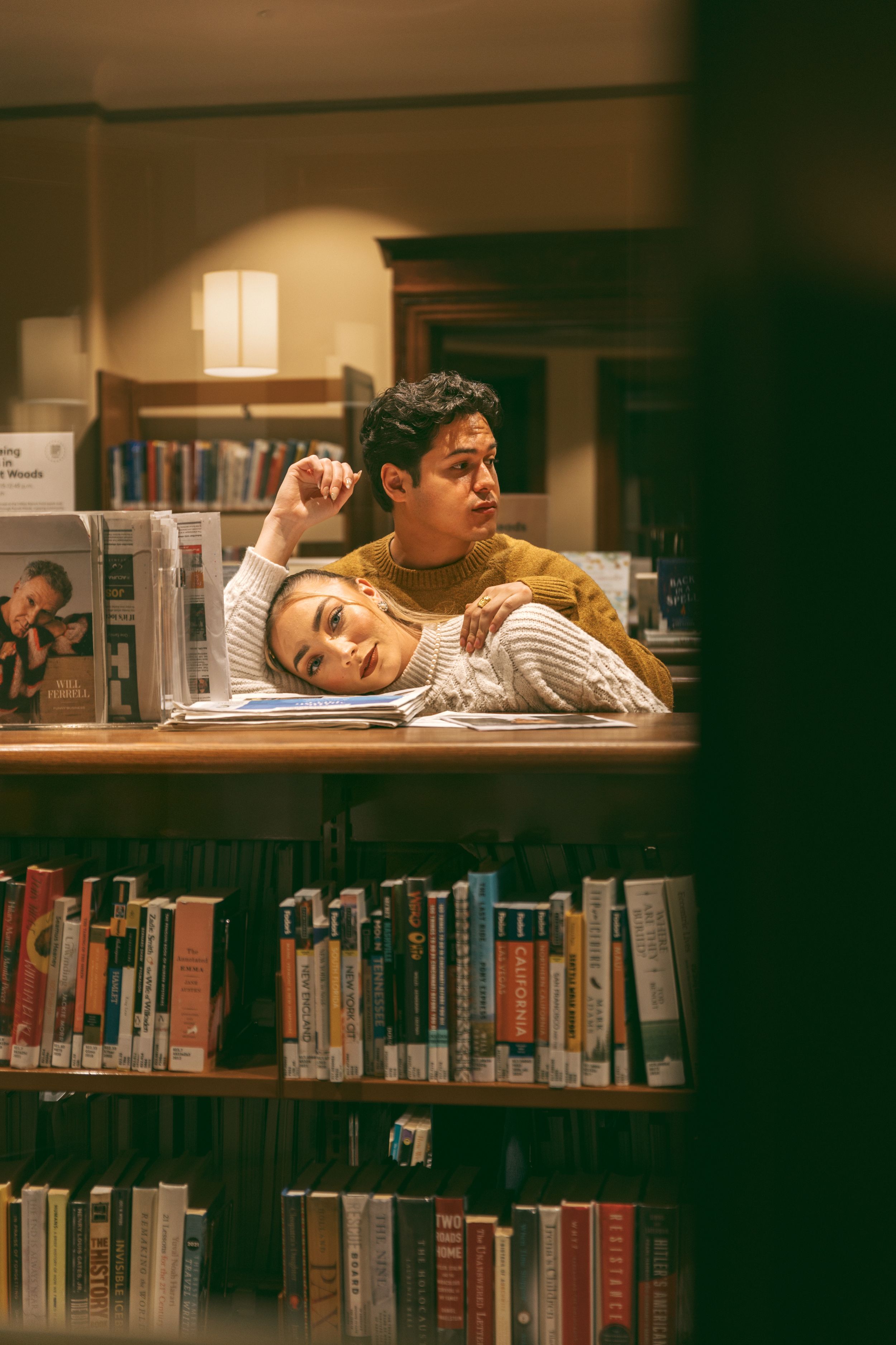 A cozy couple studying together at a library desk surrounded by books in warm lighting.