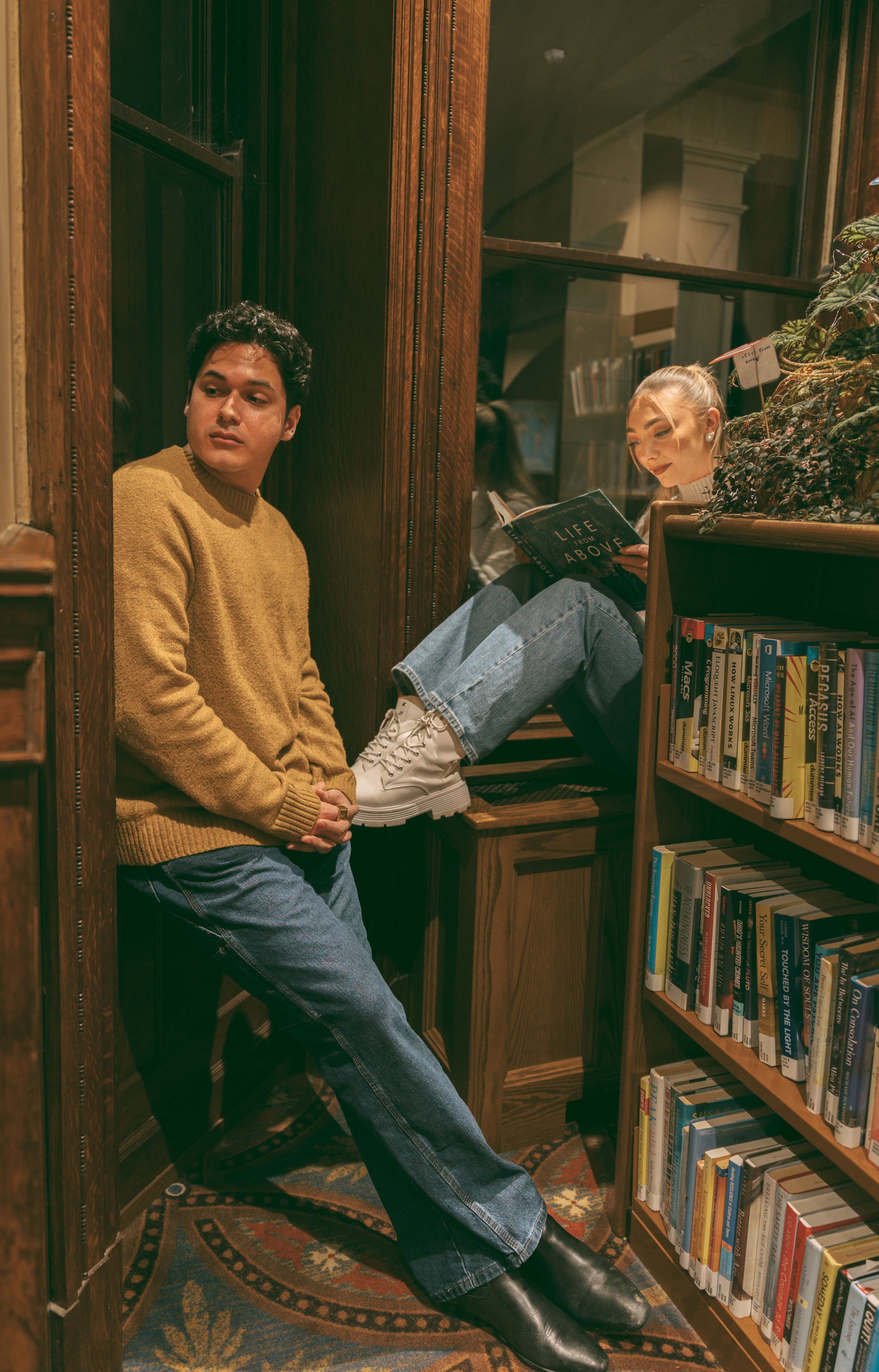 A couple poses playfully between library bookshelves in a vintage-styled photoshoot.