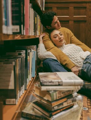 Pair resting together on floor of library with stacks of books nearby.