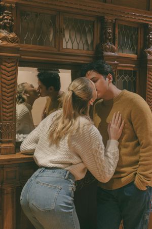 Romantic couple embracing against vintage wooden library cabinet with mirror.