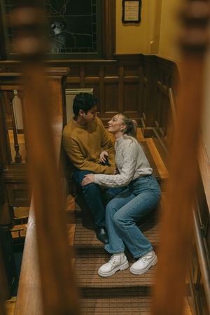 Couple sharing an intimate moment on wooden library stairs.