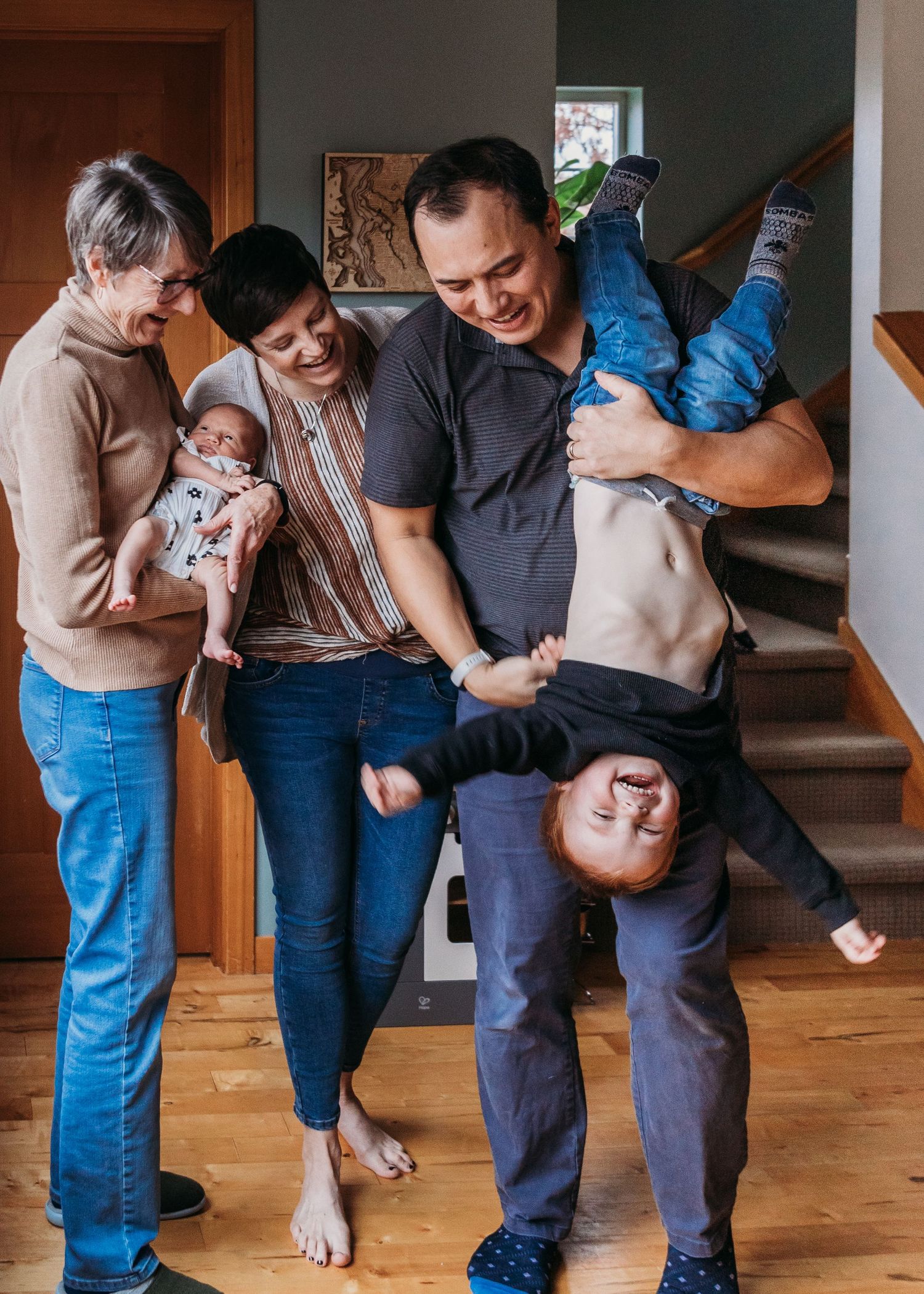 Family shares joyful moment playing and laughing together in their home hallway while holding and playing with children.
