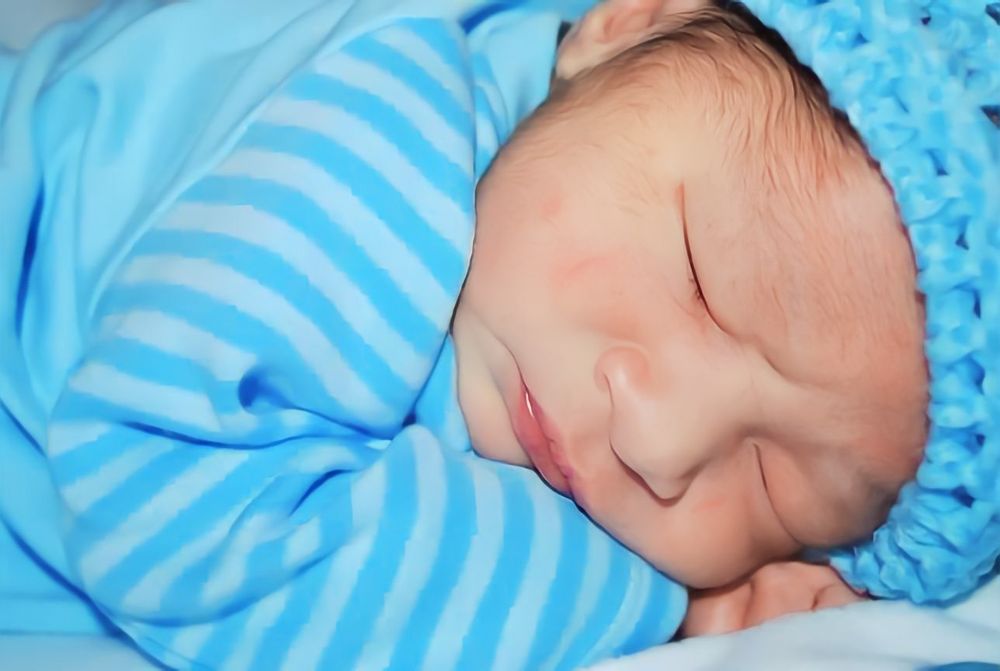 Newborn baby sleeping peacefully wrapped in blue striped blanket.