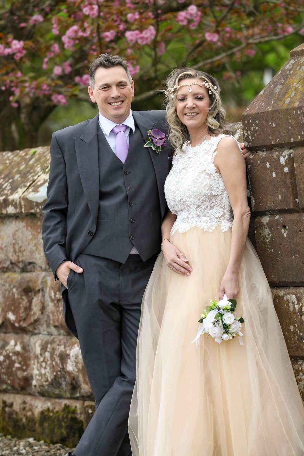 Romantic wedding portraits against stone wall with pink blossoms in background.