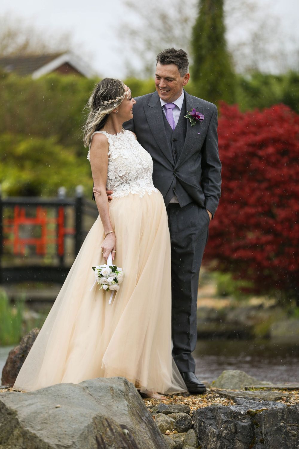 Wedding couple poses outdoors against natural scenery with red maple trees and stone wall.