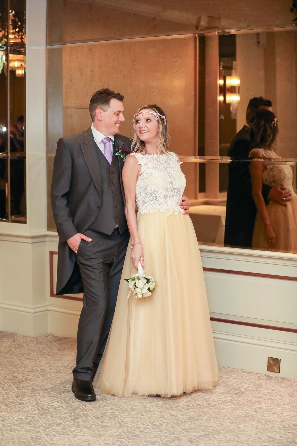 Wedding couple poses playfully in elegant indoor venue with mirrored walls.