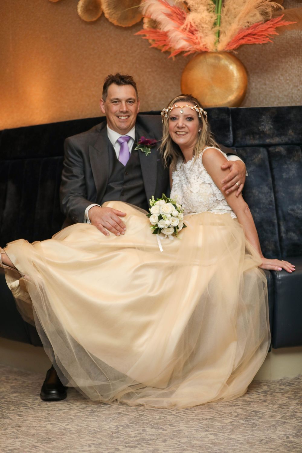 A couple poses playfully on a couch with the bride's cream-colored tulle gown spread out in sequence.