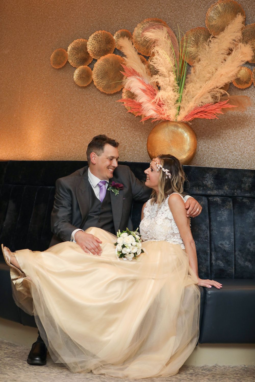 Wedding couple sitting together on brown couch with bride's champagne dress flowing.