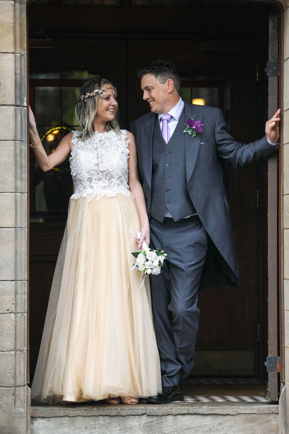 Wedding couple stands in stone doorway with natural light streaming in.