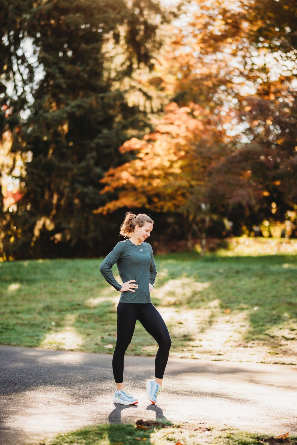 Athletic person in workout gear stretching in a park with autumn trees during golden hour sunset.