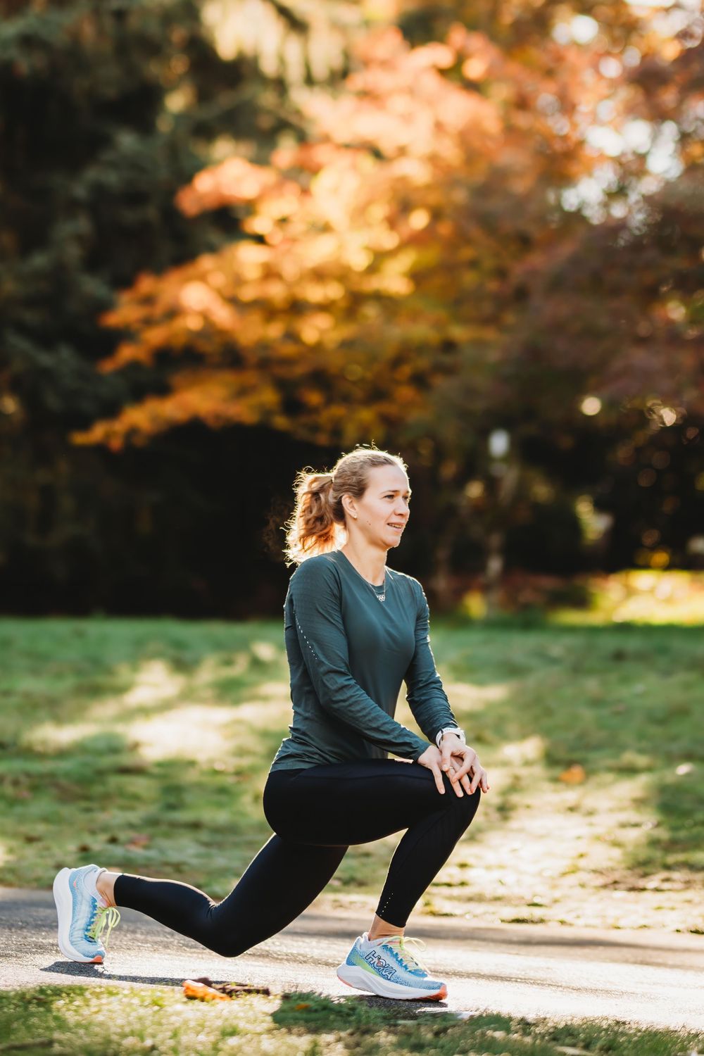 Person in black workout attire stretches outdoors during autumn with colorful fall foliage in the background beneath golden light.