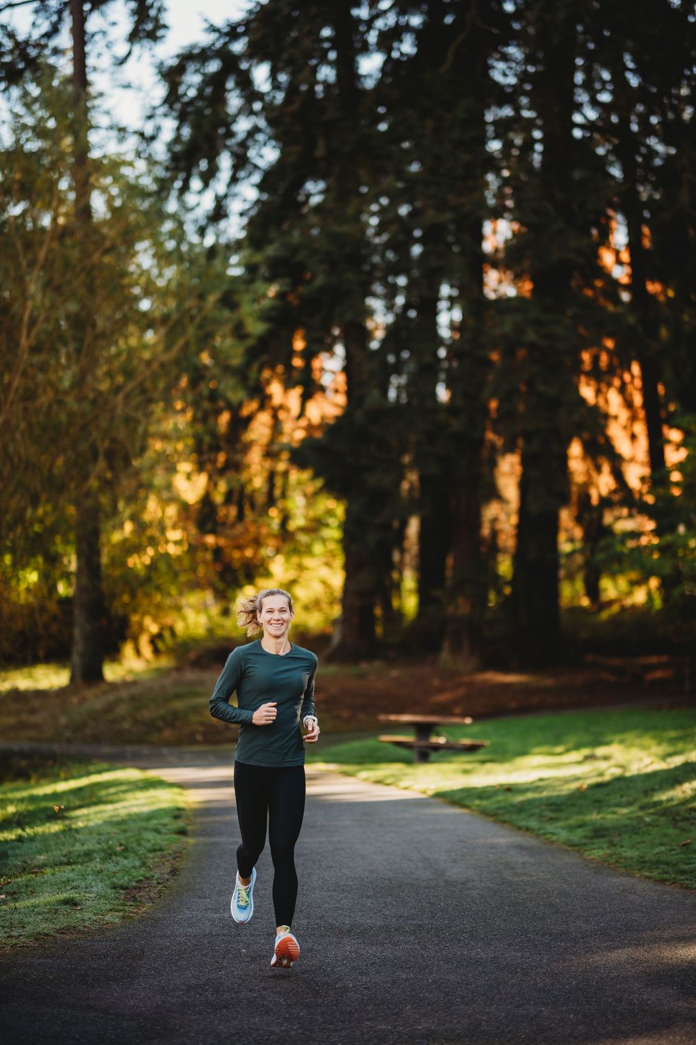 Runner jogging along scenic forest path during golden hour sunlight through tall evergreen trees.