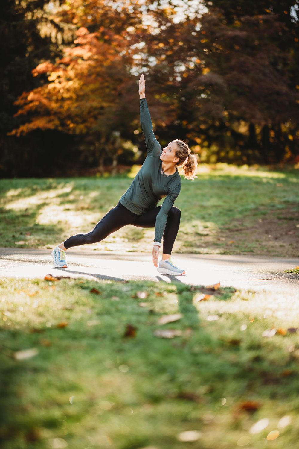 Athletic person performs outdoor yoga stretches in park during autumn with colorful foliage in background.