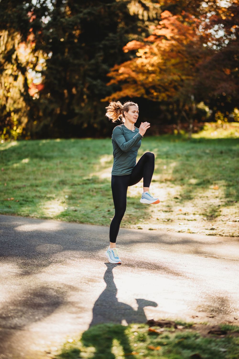 Person performing high kick exercises on a path with autumn trees in the background during golden hour light.