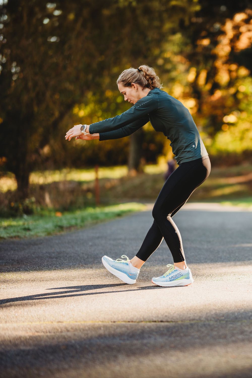 Runner performing a sequence of jumping lunges outside on a path while wearing black leggings and blue sneakers.