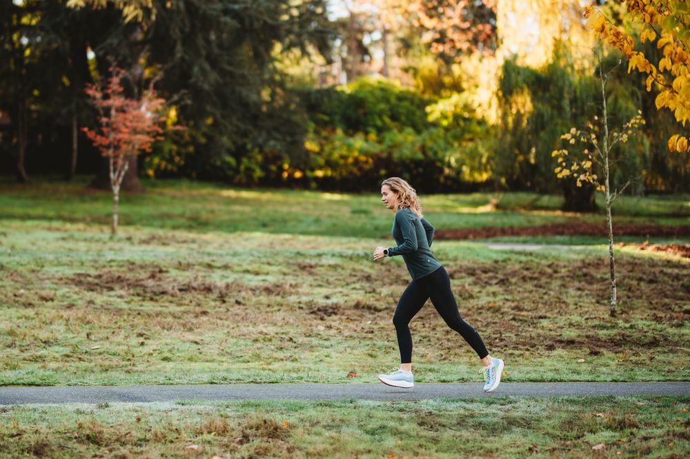 Two people walking on an autumn path surrounded by fallen leaves and trees in a park at sunset.