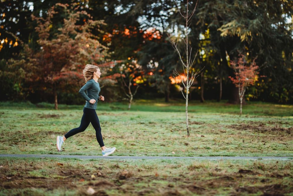 Person jogging on a trail in a park during autumn with colorful fall foliage in the background at sunset.