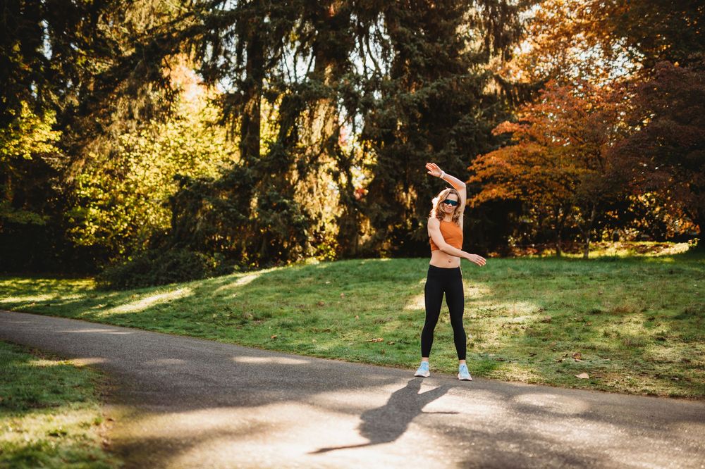A person wearing black sweatpants performs powerful jumping exercises in a sunlit autumn park setting.