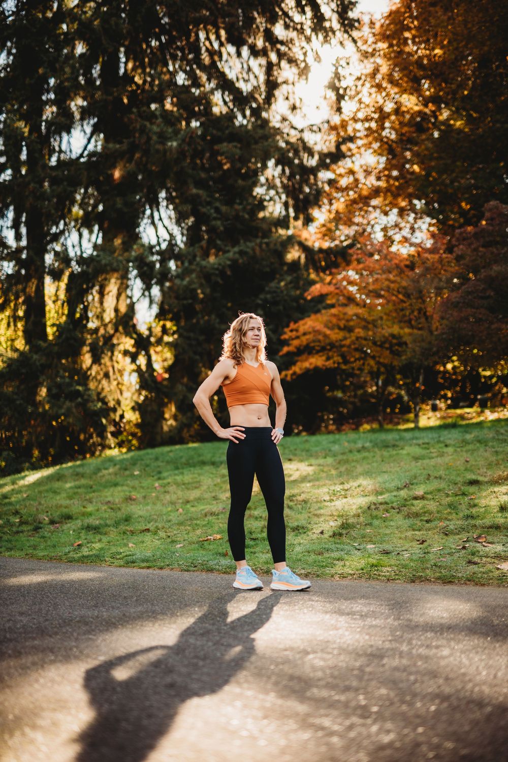 Runner in athletic wear takes a break during sunset workout on park trail surrounded by autumn trees.