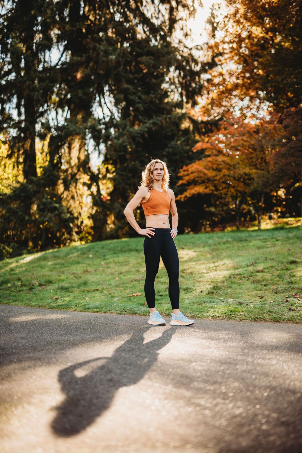 Person in orange top and black leggings exercising outdoors during golden hour sunset in a park.