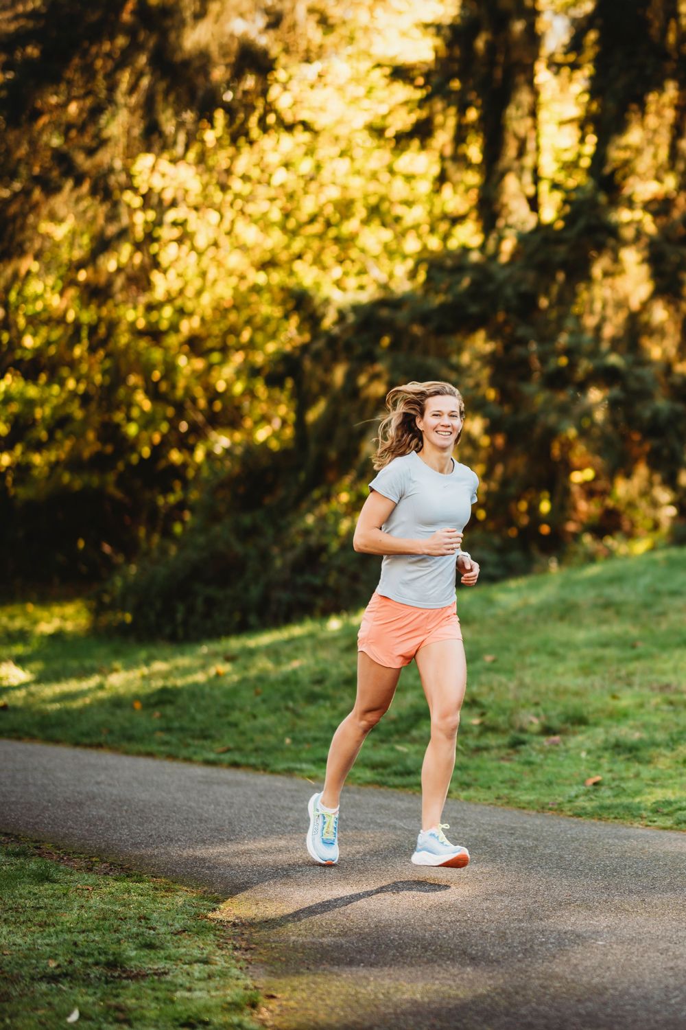 Runner on wooded trail wearing orange shorts and white t-shirt exercising at golden hour in park setting.
