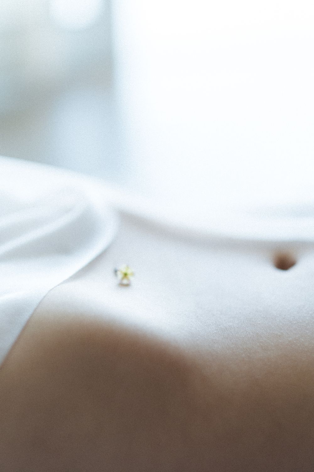 Extreme close-up macro photograph showing a tiny gold stud earring on a soft white surface.