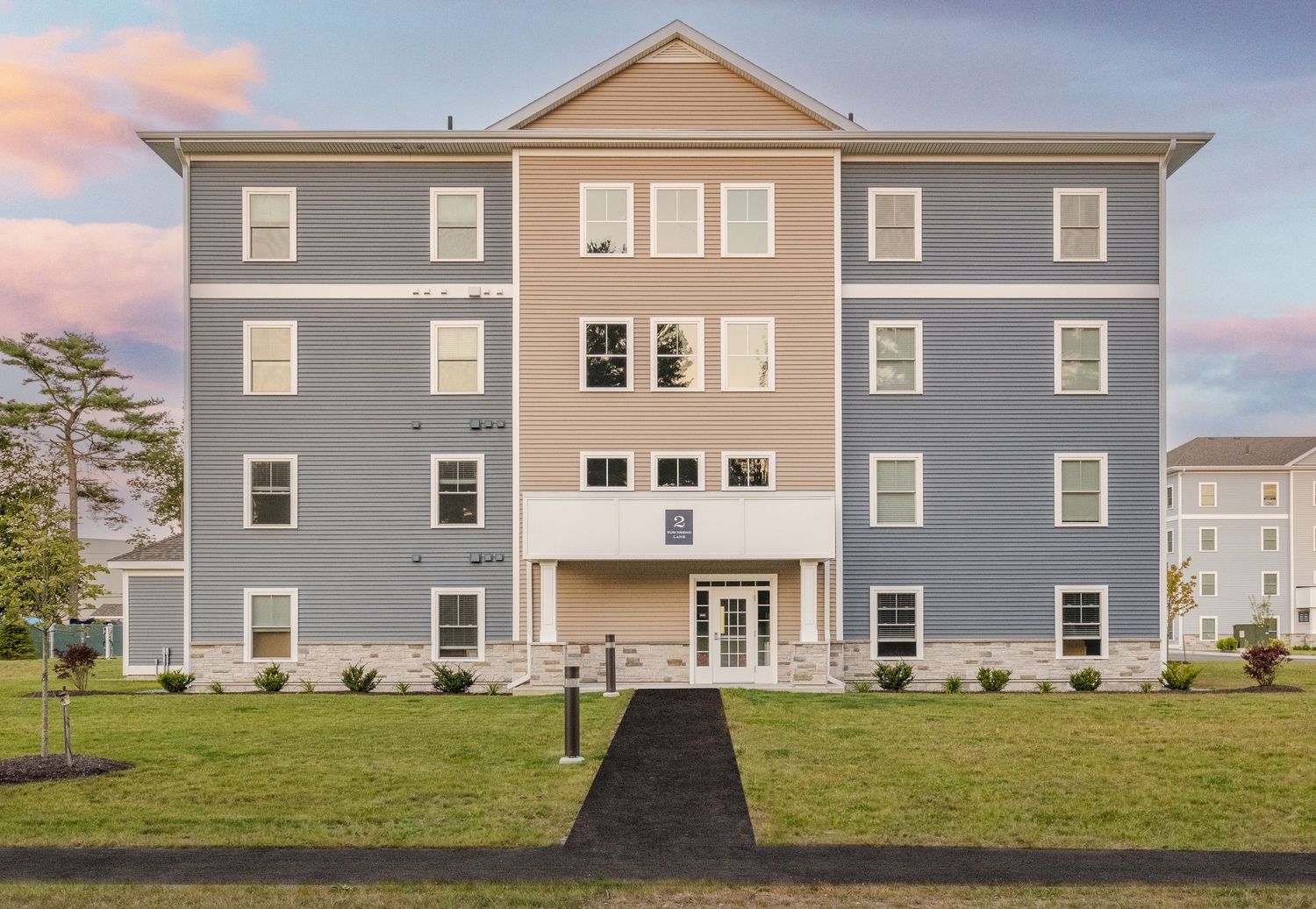 A panoramic sequence of modern gray apartment buildings with symmetrical windows and doors against a cloudy sky at sunset.